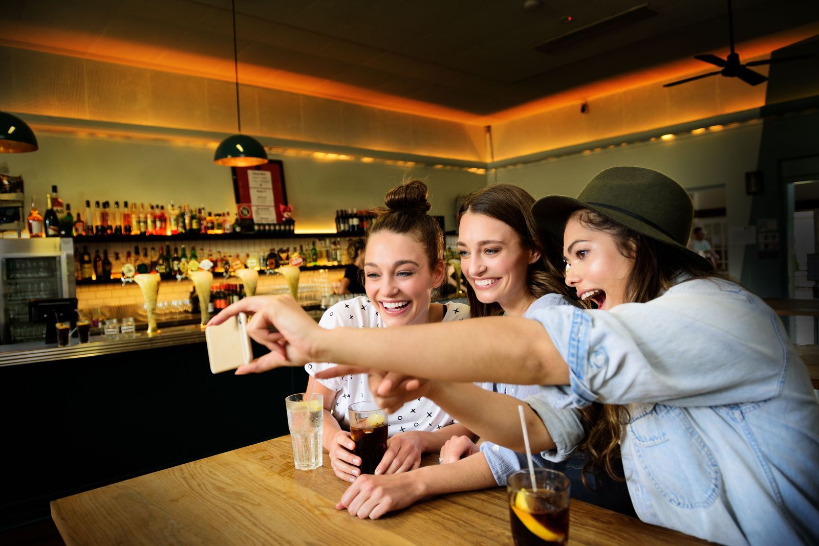 Three friends taking a selfie with drinks at a bar counter
